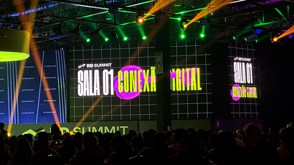 Palestra na sala de conexão digital do RD Summit 2024, com telão iluminado e público atento