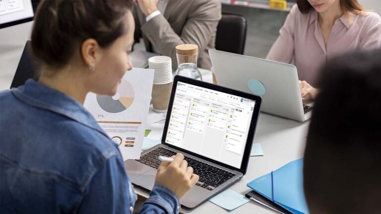Equipe analisando dados em laptop com sistema de CRM e relatórios de marketing em ambiente corporativo.